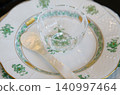 A scene of tableware consisting of a glass dish and a silver spoon on a white porcelain plate on a table. 140997464