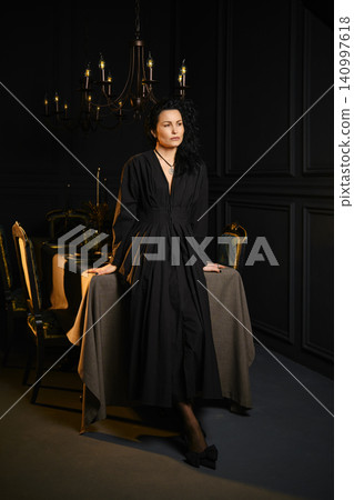 Woman in black dress stands on table in dark room with candles Woman in black dress stands on table in dark room with candles 140997618