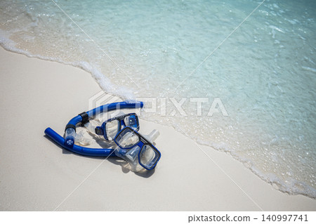 Snorkel mask on a wet shimmering sand shoreline. Turquoise water washing over a sunny beach. Tropical summer adventure for travel vacation background Snorkel mask on a wet shimmering sand shoreline. Turquoise water washing over a sunny beach. Tropical summer adventure for travel vacation background 140997741