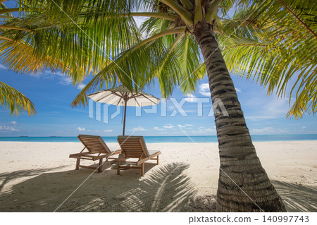 Sun loungers facing a calm turquoise lagoon. Palm trees and red umbrella on pristine sand. Luxury tropical resort for travel destination summer holiday Sun loungers facing a calm turquoise lagoon. Palm trees and red umbrella on pristine sand. Luxury tropical resort for travel destination summer holiday 140997743