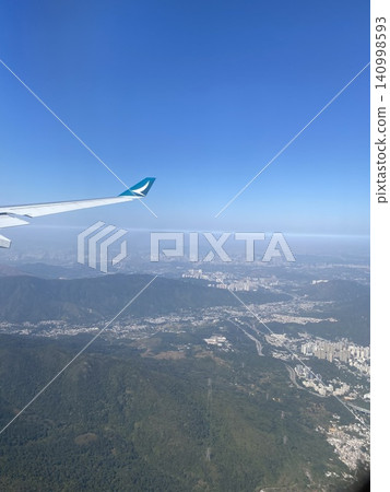 The wing of an airplane overlooking the landscape stretching from the mountain range to the city. The wing of an airplane overlooking the landscape stretching from the mountain range to the city. 140998593