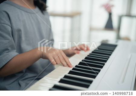 Child practicing piano with focused hands pressing keys on white keyboard in bright indoor environment learning music instrument Child practicing piano with focused hands pressing keys on white keyboard in bright indoor environment learning music instrument 140998718