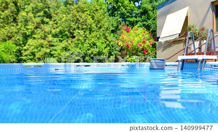 Large swimming pool set in the backyard next to the house. Large swimming pool set in the backyard next to the house. 140999477