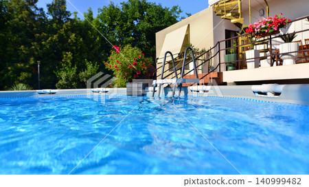 Large swimming pool set in the backyard next to the house. Large swimming pool set in the backyard next to the house. 140999482