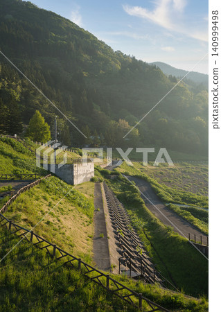 The lush green slopes of Sagae Dam and the surrounding mountains are bathed in the soft morning light. The lush green slopes of Sagae Dam and the surrounding mountains are bathed in the soft morning light. 140999498