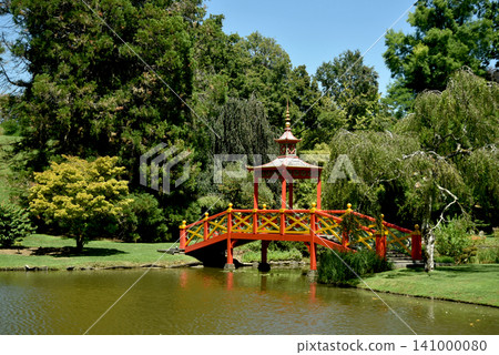 Traditional red Japanese bridge crossing a peaceful pond in a beautiful botanical garden. Scenic landscape with lush trees, calm water and elegant oriental architecture on a sunny day. Traditional red Japanese bridge crossing a peaceful pond in a beautiful botanical garden. Scenic landscape with lush trees, calm water and elegant oriental architecture on a sunny day. 141000080