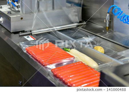 Automated vacuum packaging machine sealing fresh sausages on conveyor line in food processing factory plant Automated vacuum packaging machine sealing fresh sausages on conveyor line in food processing factory plant 141000488