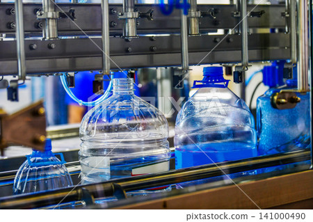 Automated water bottling machine filling large plastic bottles on conveyor belt in beverage production factory plant Automated water bottling machine filling large plastic bottles on conveyor belt in beverage production factory plant 141000490