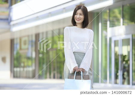 一位三十多歲的微笑的女子手提購物袋，享受著戶外生活方式。 141000672