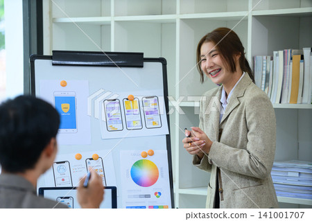 Young Gen Z Female UI UX Designer Presenting Mobile App Wireframe and Color Palette on Whiteboard in Modern Office Young Gen Z Female UI UX Designer Presenting Mobile App Wireframe and Color Palette on Whiteboard in Modern Office 141001707
