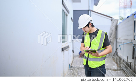 Young Asian Construction Inspector Engineer Using Digital Tablet on Building Site Wearing Safety Vest and Hardhat 141001765
