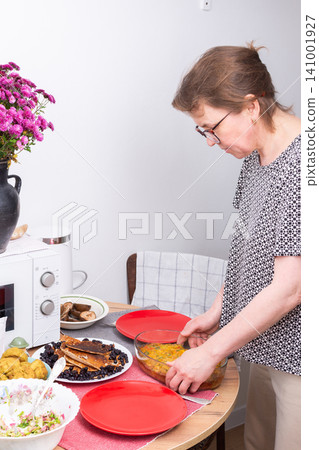 A woman sets plates on a table for breakfast. She arranges food like pie and pancakes, salad, and other dishes in a casual dining area during the morning hours A woman sets plates on a table for breakfast. She arranges food like pie and pancakes, salad, and other dishes in a casual dining area during the morning hours 141001927