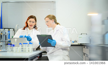 Two Female Scientists Collaborating in Modern Laboratory with Test Tubes and Clipboard Two Female Scientists Collaborating in Modern Laboratory with Test Tubes and Clipboard 141001966