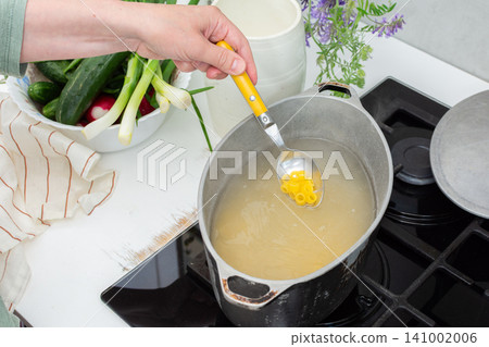 A woman stirs gluten-free noodles in a pot on the stove. Fresh vegetables are placed on the counter while water boils in the pot. The kitchen is busy and bright A woman stirs gluten-free noodles in a pot on the stove. Fresh vegetables are placed on the counter while water boils in the pot. The kitchen is busy and bright 141002006
