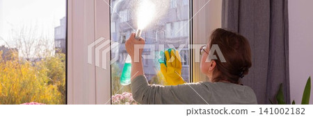 A person is washing windows in an apartment on a balcony filled with flowers. This activity takes place in fall as winter approaches, preparing for the colder months A person is washing windows in an apartment on a balcony filled with flowers. This activity takes place in fall as winter approaches, preparing for the colder months 141002182