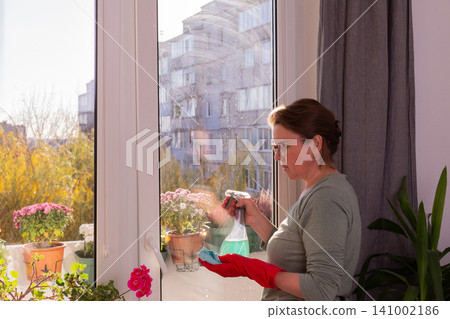 A person cleans windows in a city apartment on a balcony. The scene shows autumn flowers and a clear view outside on a sunny day as winter approaches A person cleans windows in a city apartment on a balcony. The scene shows autumn flowers and a clear view outside on a sunny day as winter approaches 141002186