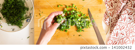 A person is preparing a salad by chopping fresh green vegetables on a wooden cutting board. Organic produce is used to make a healthy meal in a sunny kitchen A person is preparing a salad by chopping fresh green vegetables on a wooden cutting board. Organic produce is used to make a healthy meal in a sunny kitchen 141002432
