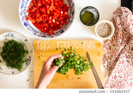 A person is preparing a salad by chopping fresh green vegetables on a wooden cutting board. Organic produce is used to make a healthy meal in a sunny kitchen A person is preparing a salad by chopping fresh green vegetables on a wooden cutting board. Organic produce is used to make a healthy meal in a sunny kitchen 141002437
