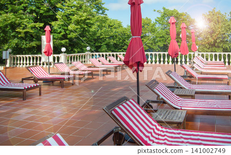 Empty wooden deck chairs with red and white striped mattresses stand in a row. Luxury outdoor recreation, sunshine Empty wooden deck chairs with red and white striped mattresses stand in a row. Luxury outdoor recreation, sunshine 141002749