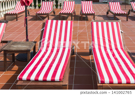 Empty wooden deck chairs with red and white striped mattresses stand in a row. Luxury outdoor recreation, sunshine Empty wooden deck chairs with red and white striped mattresses stand in a row. Luxury outdoor recreation, sunshine 141002765