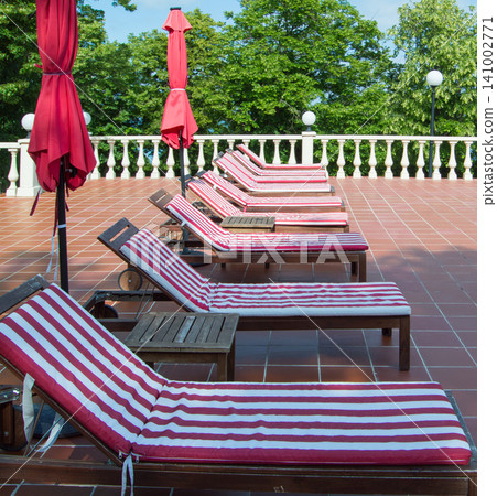 Empty wooden deck chairs with red and white striped mattresses stand in a row. Luxury sunshine Empty wooden deck chairs with red and white striped mattresses stand in a row. Luxury sunshine 141002771