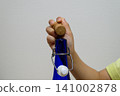 A hand opening the cork stopper of a blue glass bottle 141002878