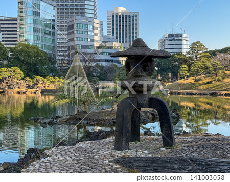 A Japanese garden scene featuring a stone lantern and snow-covered trees, set against the backdrop of city skyscrapers. A Japanese garden scene featuring a stone lantern and snow-covered trees, set against the backdrop of city skyscrapers. 141003058