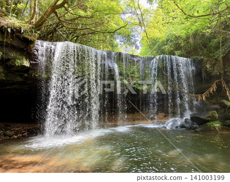 The scenery of Nabegataki waterfall in Minamioguni Town, Kumamoto Prefecture, surrounded by lush green trees and flowing from behind. The scenery of Nabegataki waterfall in Minamioguni Town, Kumamoto Prefecture, surrounded by lush green trees and flowing from behind. 141003199