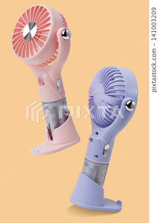 Two pastel pink and purple portable misting fans flying or levitating in the air on isolated beige background, summer levitation concept Two pastel pink and purple portable misting fans flying or levitating in the air on isolated beige background, summer levitation concept 141003209