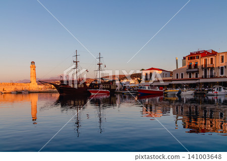Beautiful sunset over a harbor with traditional boats in a historic coastal town 141003648