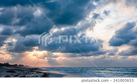 Beautiful sunset over the beach with dramatic clouds and shimmering ocean waves Beautiful sunset over the beach with dramatic clouds and shimmering ocean waves 141003653