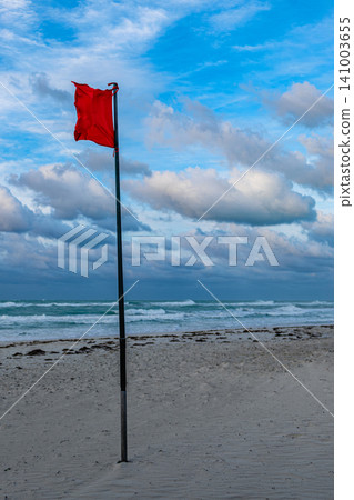 Red warning flag standing tall on a beach with cloudy skies and waves Red warning flag standing tall on a beach with cloudy skies and waves 141003655