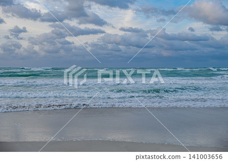 Waves crash on the shore under a cloudy sky at twilight on a beach Waves crash on the shore under a cloudy sky at twilight on a beach 141003656