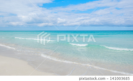 Calm ocean waves gently lap on the sandy shore under a bright blue sky 141003685