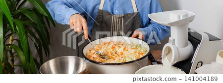 A 53-year-old man mixes cabbage and carrots in a large bowl in his kitchen while preparing for fermentation using simple tools and ingredients, banner A 53-year-old man mixes cabbage and carrots in a large bowl in his kitchen while preparing for fermentation using simple tools and ingredients, banner 141004189