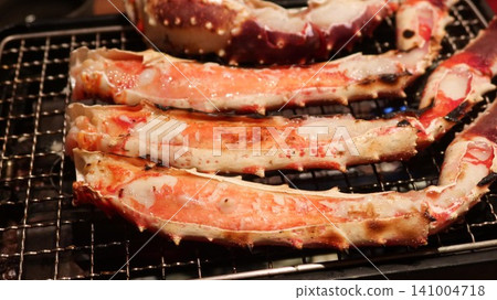 close up of four Grilled king crab legs sizzling on a metal wire rack over an open flame. These split crab legs showcase tender, juicy white and pink meat with beautiful char marks from grilling. close up of four Grilled king crab legs sizzling on a metal wire rack over an open flame. These split crab legs showcase tender, juicy white and pink meat with beautiful char marks from grilling. 141004718