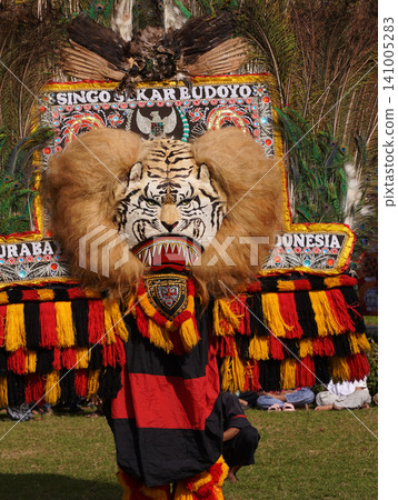 SURABAYA, INDONESIA - JULY 5, 2026: A performer wears the heavy Singo Barong tiger and peacock feather mask with 'Singo Sekar Budoyo' text during a traditional Reog Ponorogo cultural dance performance SURABAYA, INDONESIA - JULY 5, 2026: A performer wears the heavy Singo Barong tiger and peacock feather mask with 'Singo Sekar Budoyo' text during a traditional Reog Ponorogo cultural dance performance 141005283