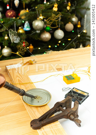 Fixing the wires of a Christmas tree garland. Tools like pliers and scissors are on the table. Electrical parts are laid out for repair Fixing the wires of a Christmas tree garland. Tools like pliers and scissors are on the table. Electrical parts are laid out for repair 141005412