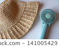 Using a portable fan and a straw hat to cope with the heat. 141005429