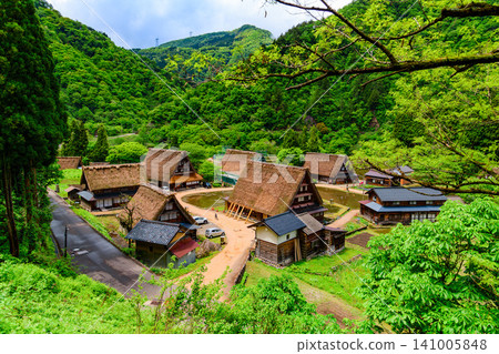 在一個晴朗的初夏日子裡,從觀景點可以看到遠處菅沼合掌造村莊五箇山,一個孩子騎著自行車沿著街道行駛。 在一個晴朗的初夏日子裡,從觀景點可以看到遠處菅沼合掌造村莊五箇山,一個孩子騎著自行車沿著街道行駛。 141005848