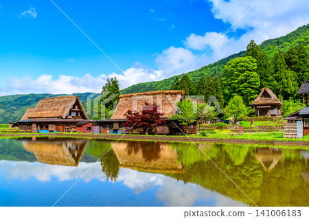 在一個晴朗的初夏日子裡,五箇山合掌造村的合掌造房屋倒映在水稻田中,景色十分美麗。 在一個晴朗的初夏日子裡,五箇山合掌造村的合掌造房屋倒映在水稻田中,景色十分美麗。 141006183