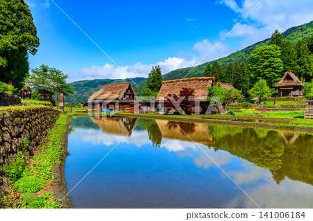 在一個晴朗的初夏日子裡,五箇山合掌造村的合掌造房屋倒映在水稻田中,景色十分美麗。 在一個晴朗的初夏日子裡,五箇山合掌造村的合掌造房屋倒映在水稻田中,景色十分美麗。 141006184