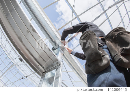 Installation work on the framework of a glass greenhouse (viewed from above) Installation work on the framework of a glass greenhouse (viewed from above) 141006443