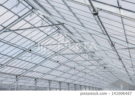 A photograph of a greenhouse with a glass roof and steel frame, taken from a low-angle perspective. A photograph of a greenhouse with a glass roof and steel frame, taken from a low-angle perspective. 141006487