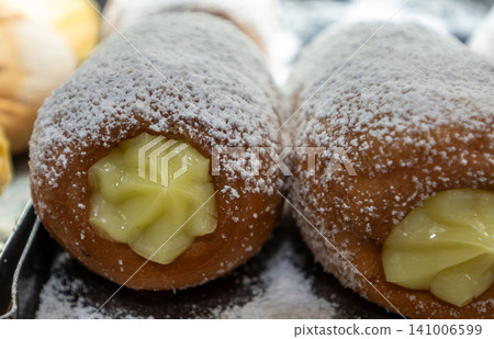 Naples, italy. December 27, 2024. Sweet neapolitan bomboloni donut, a traditional dessert, topped with powdered sugar and filled with yellow cream Naples, italy. December 27, 2024. Sweet neapolitan bomboloni donut, a traditional dessert, topped with powdered sugar and filled with yellow cream 141006599