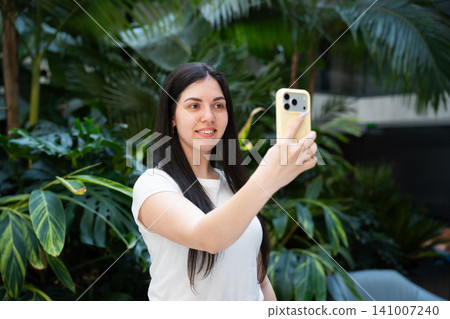 Young woman taking a selfie in lush green garden environment. Social media content creation and personal branding 141007240