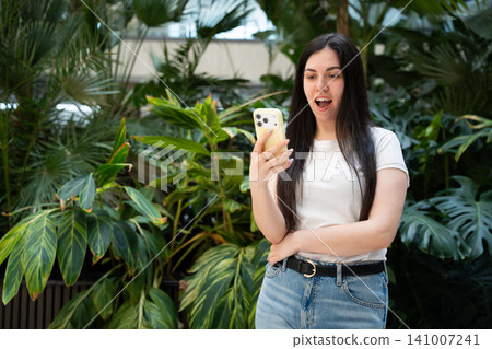 Young woman using smartphone in a vibrant green office environment. Mobile communication smartphone technology and digital lifestyle Young woman using smartphone in a vibrant green office environment. Mobile communication smartphone technology and digital lifestyle 141007241