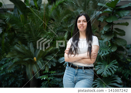 Young professional woman standing confidently in a lush green office environment. Workplace wellbeing and sustainable corporate design 141007242