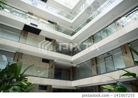 Modern office atrium with glass roof and indoor garden showcasing corporate architecture. Sustainable workplace design and biophilic interior environment Modern office atrium with glass roof and indoor garden showcasing corporate architecture. Sustainable workplace design and biophilic interior environment 141007255