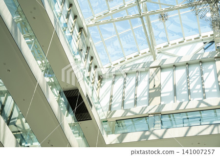 Interior view of a modern architectural glass atrium with abundant natural light. Corporate building design and contemporary workplace environment Interior view of a modern architectural glass atrium with abundant natural light. Corporate building design and contemporary workplace environment 141007257